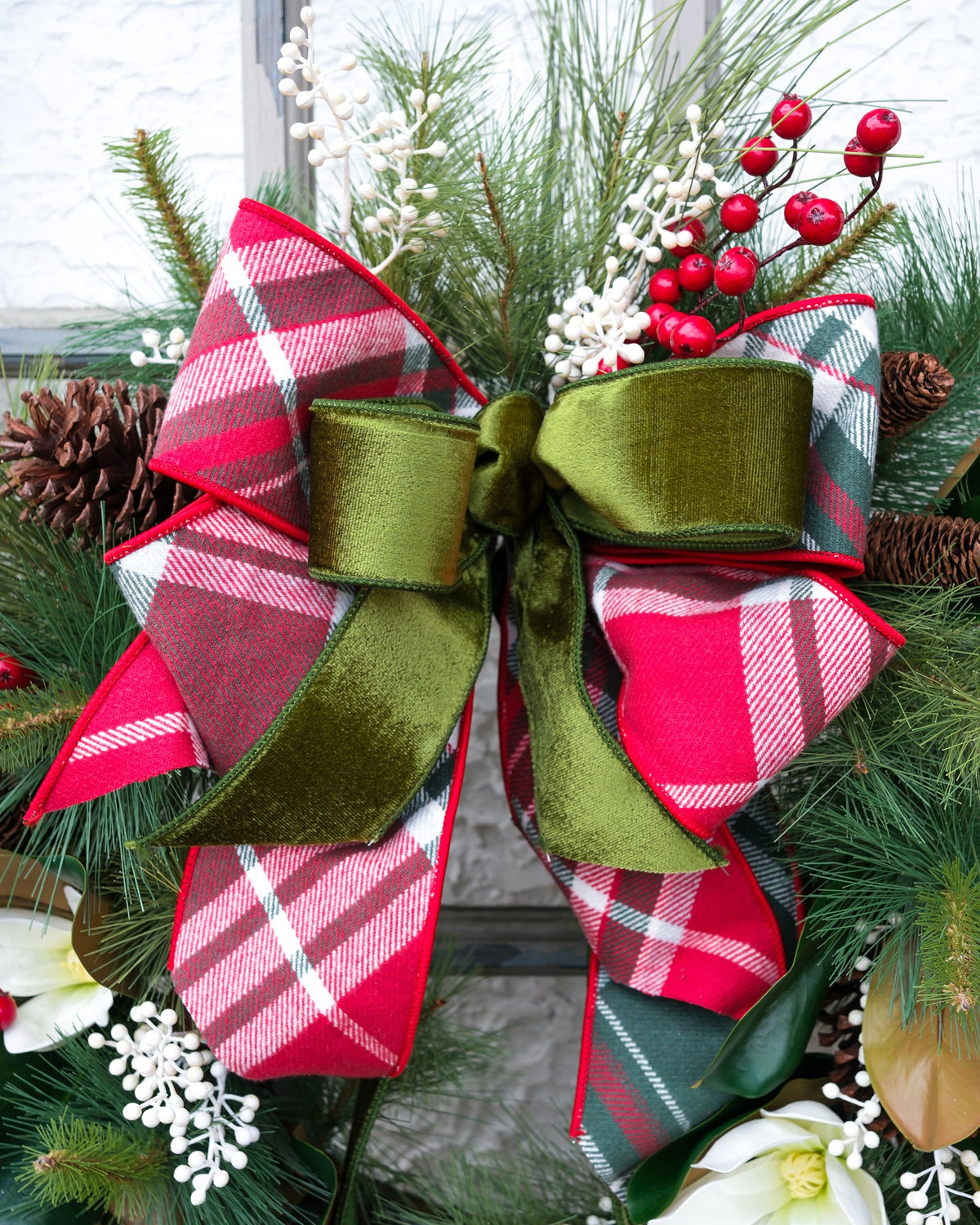 Holiday wreath close-up with big red-and-white plaid bow, pine needles, and white berry clusters