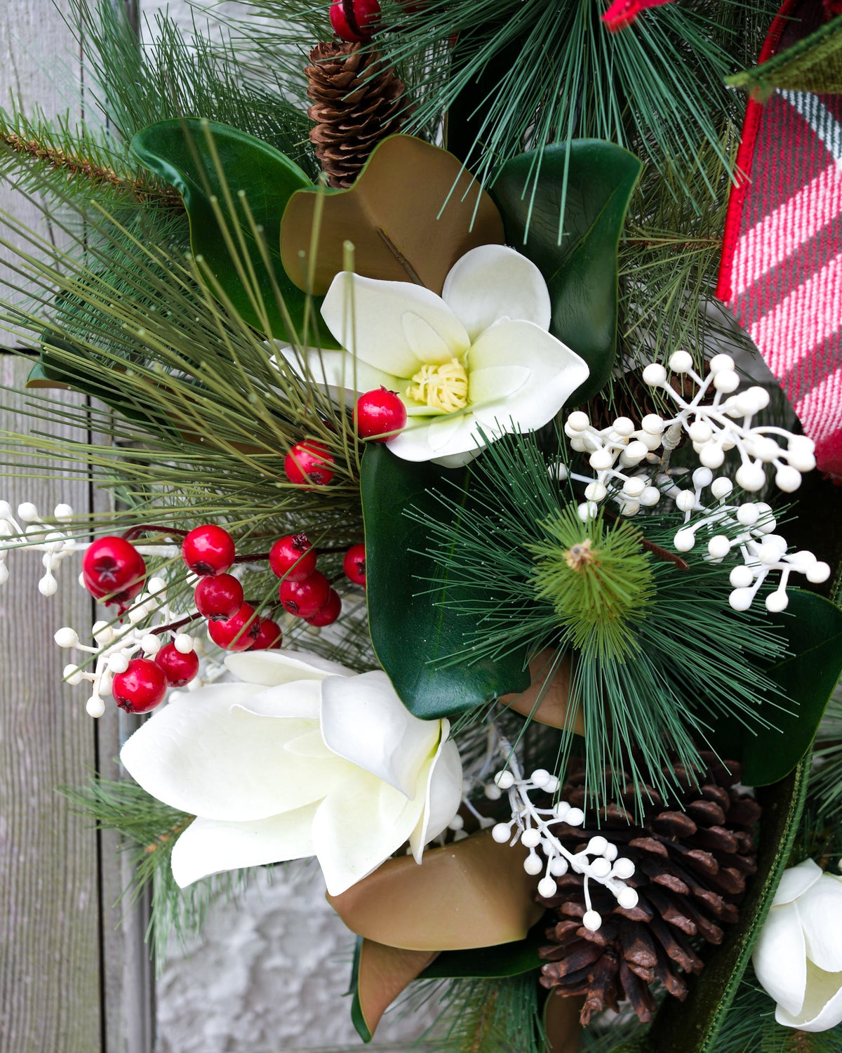 Holiday wreath close-up with white flowers, green leaves, red berries, and plaid bow edge