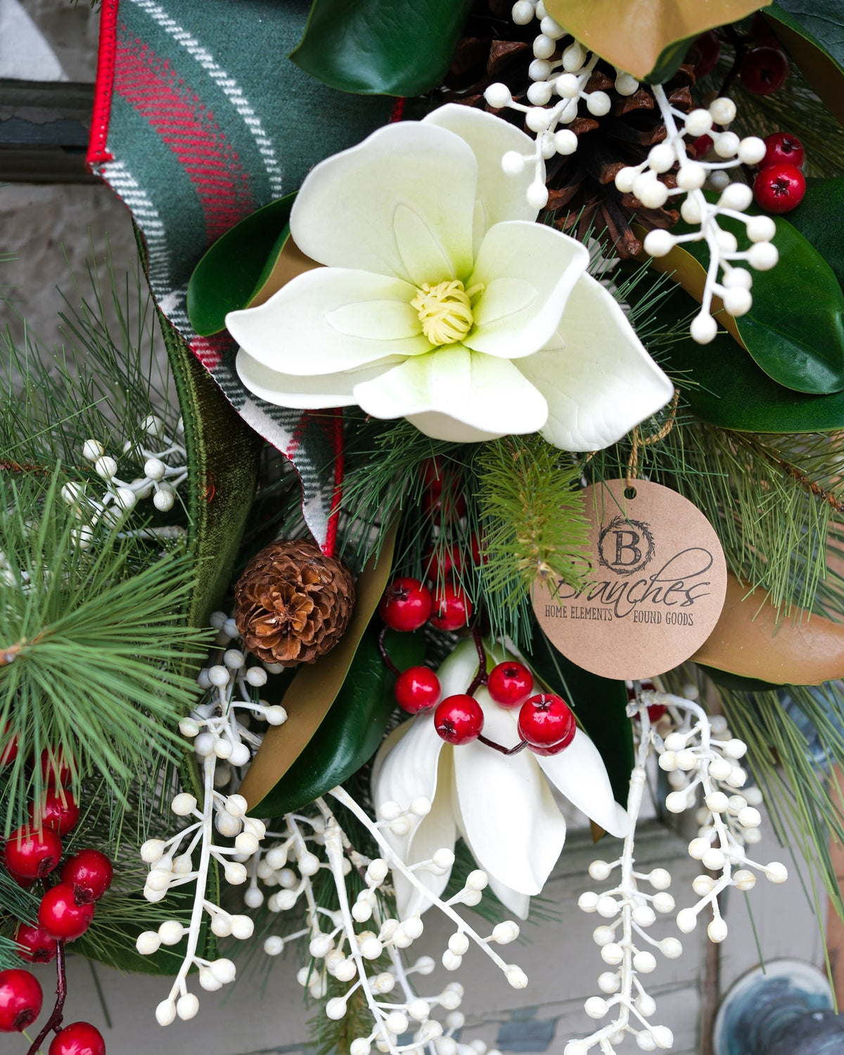 Holiday wreath close-up with white blossoms, red berries, pinecone, and decorative leaf tag