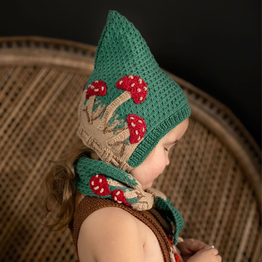 Hunter green pixie hat with red mushrooms and beige cuff, worn with ties