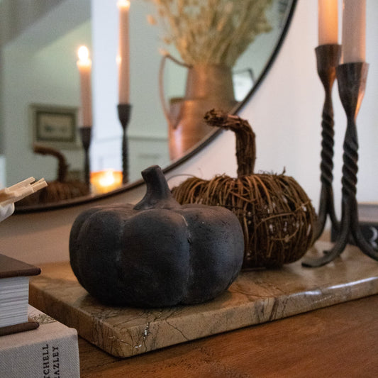 Dark decorative pumpkin on a wood tray among candles and seasonal decor