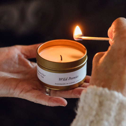 Wild Peonies candle in gold tin with lit wick, held in hands