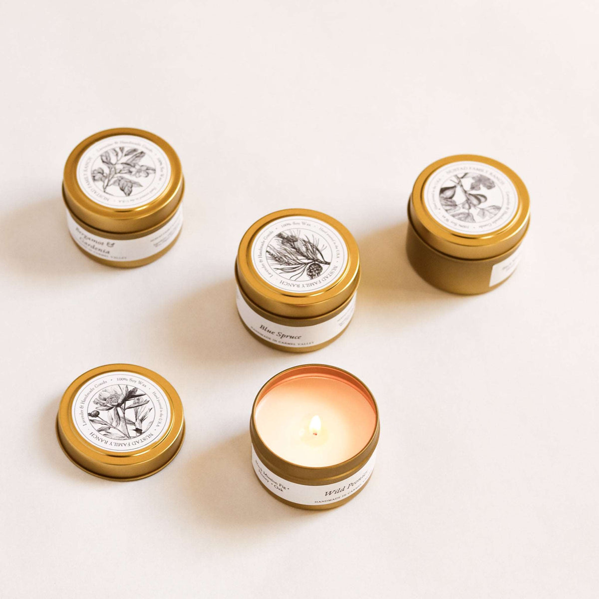 Unlit farmhouse tin candles with gold lids, cream labels (various scents)