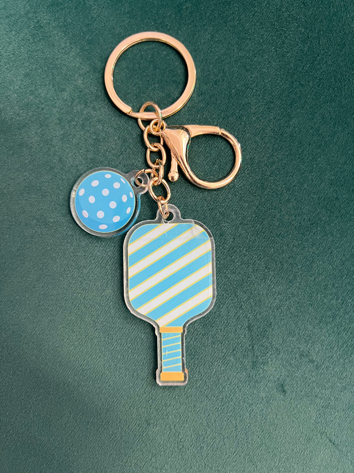 Acrylic pickleball paddle keychain with a striped blue and yellow paddle and blue ball charm