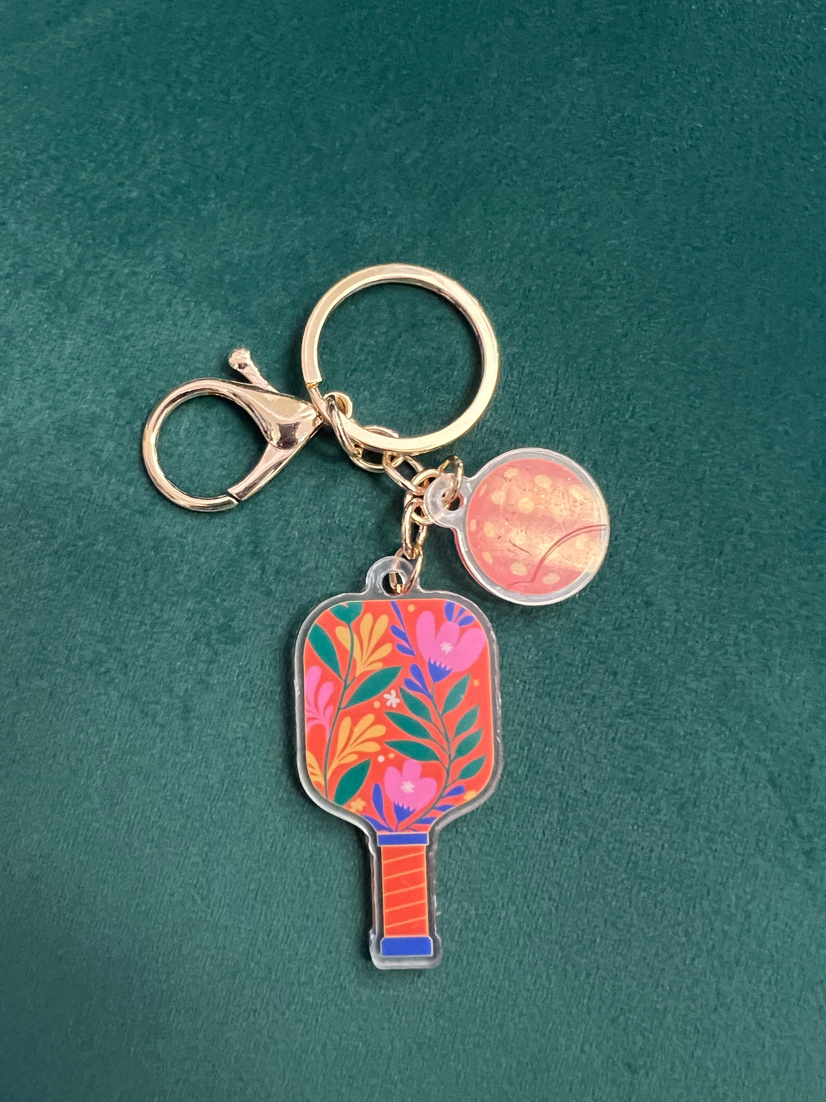 Acrylic pickleball paddle keychain with a colorful floral paddle and pink ball charm