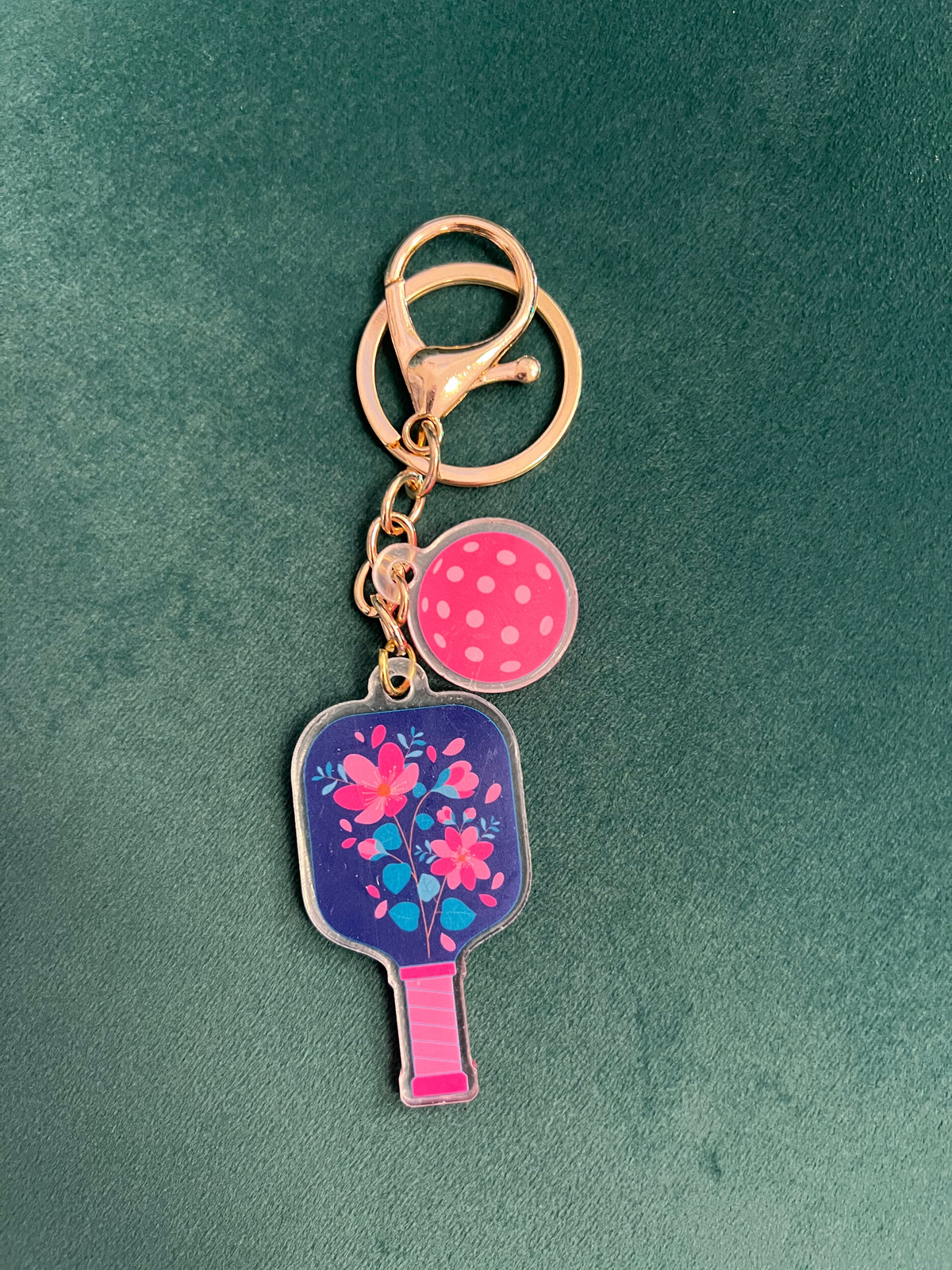 Acrylic pickleball paddle keychain with a navy floral paddle and pink-dotted ball charm