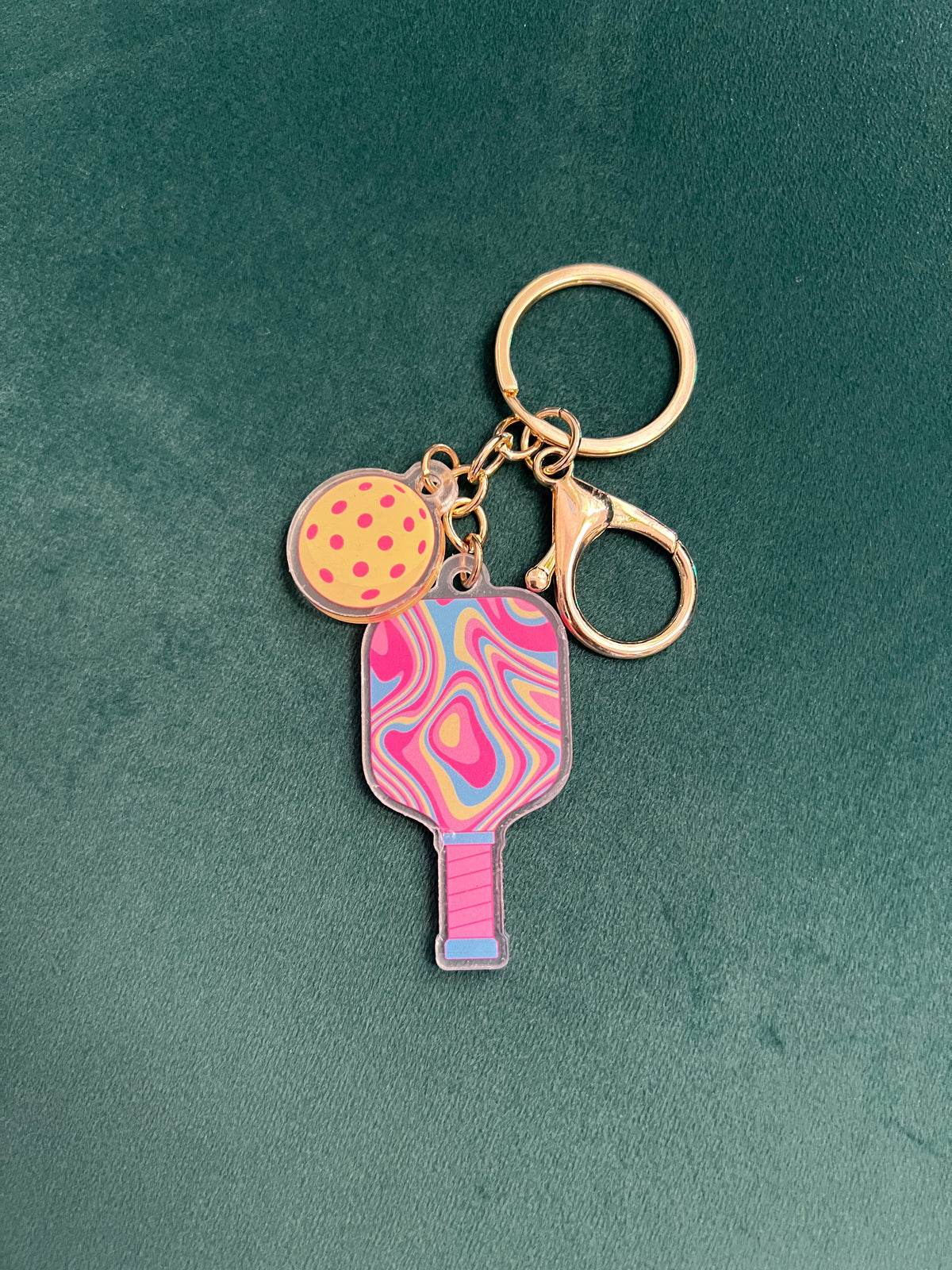 Acrylic pickleball paddle keychain with a pink and blue swirled paddle and yellow ball charm