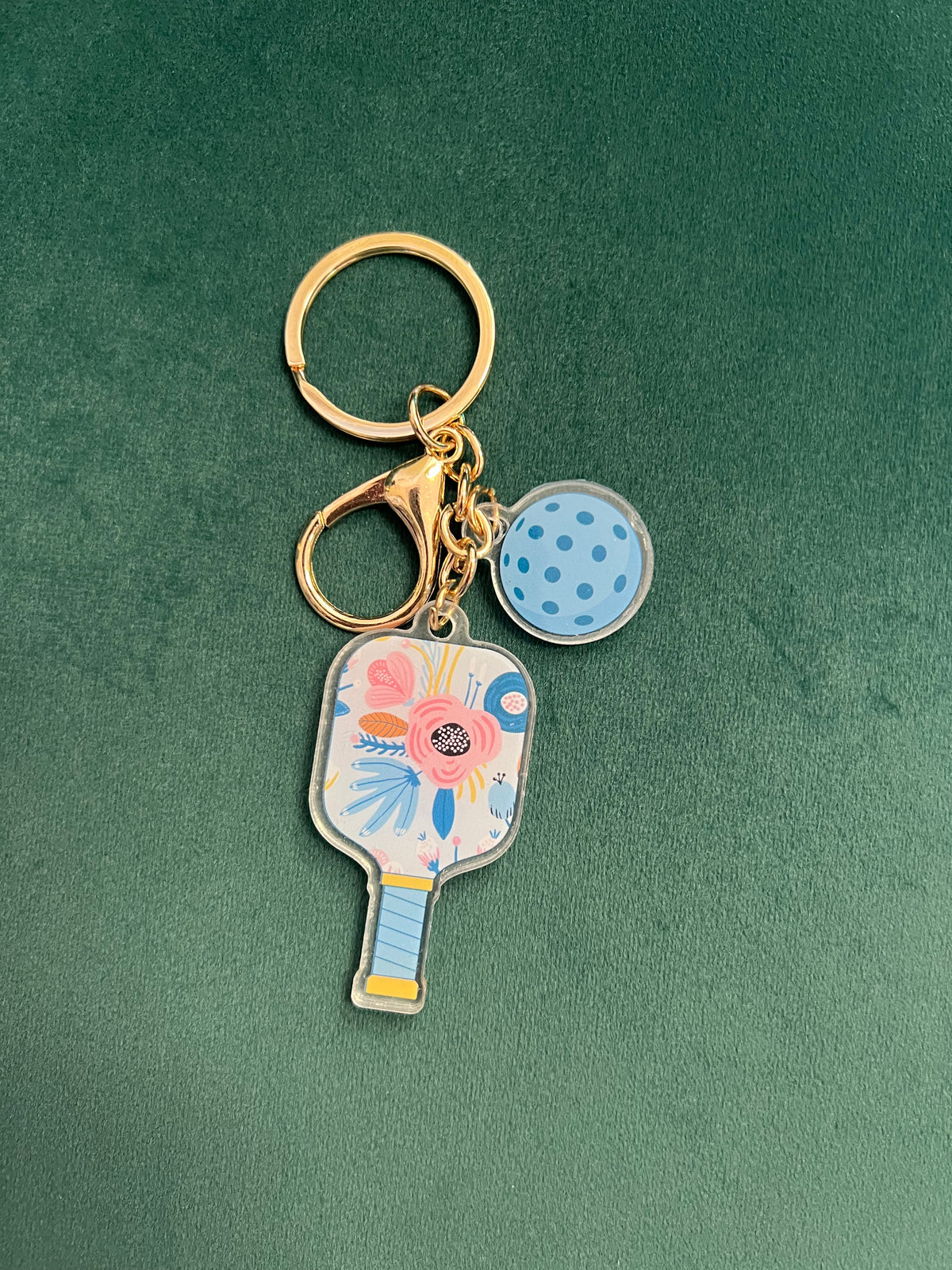Acrylic pickleball paddle keychain with a white floral paddle and blue-dotted ball charm