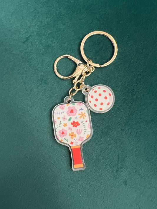 Acrylic pickleball paddle keychain with a white floral paddle and coral-dotted ball charm