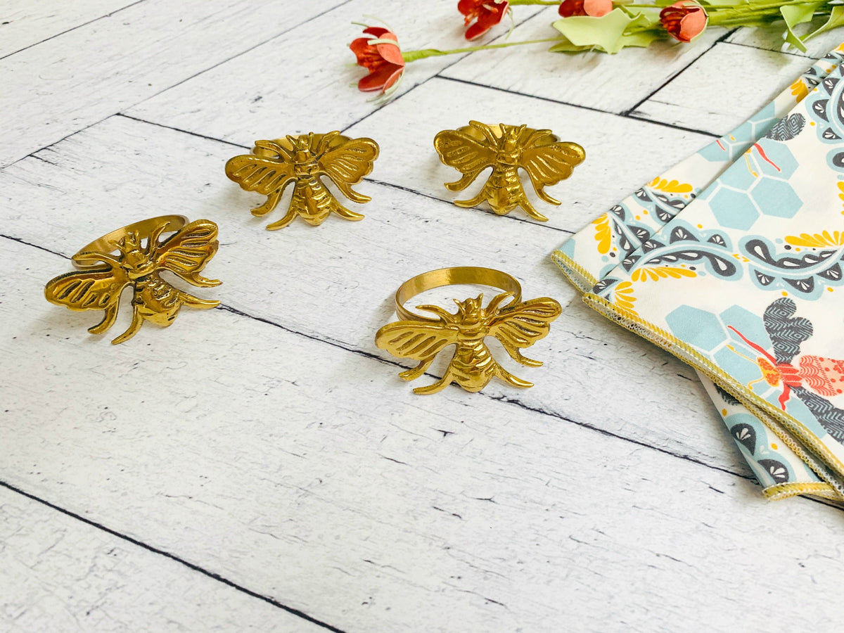 Gold bee napkin rings with a corner of bee-print cloth napkin in light blue and orange