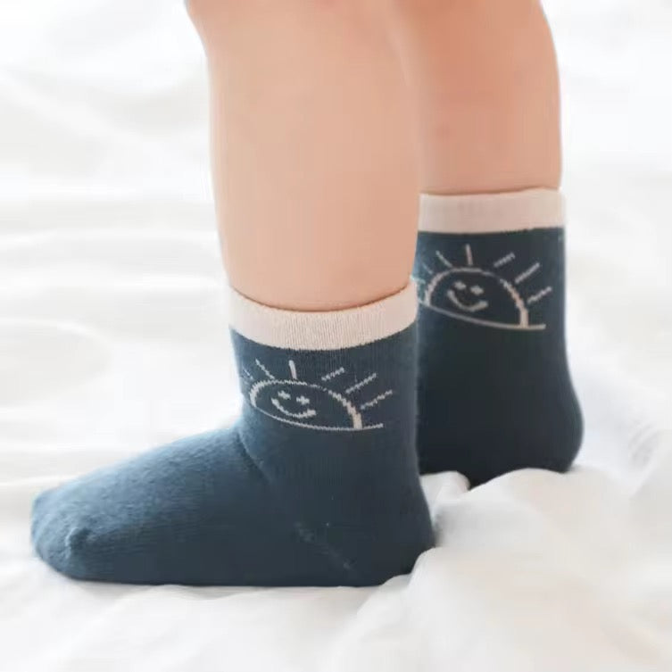Toddler socks with dark teal sides and sun face graphic, worn with bare legs