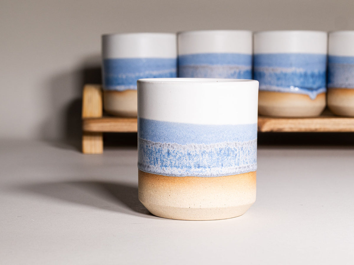 Stoneware smoothie cup with blue band and tan base, speckled glaze, on display