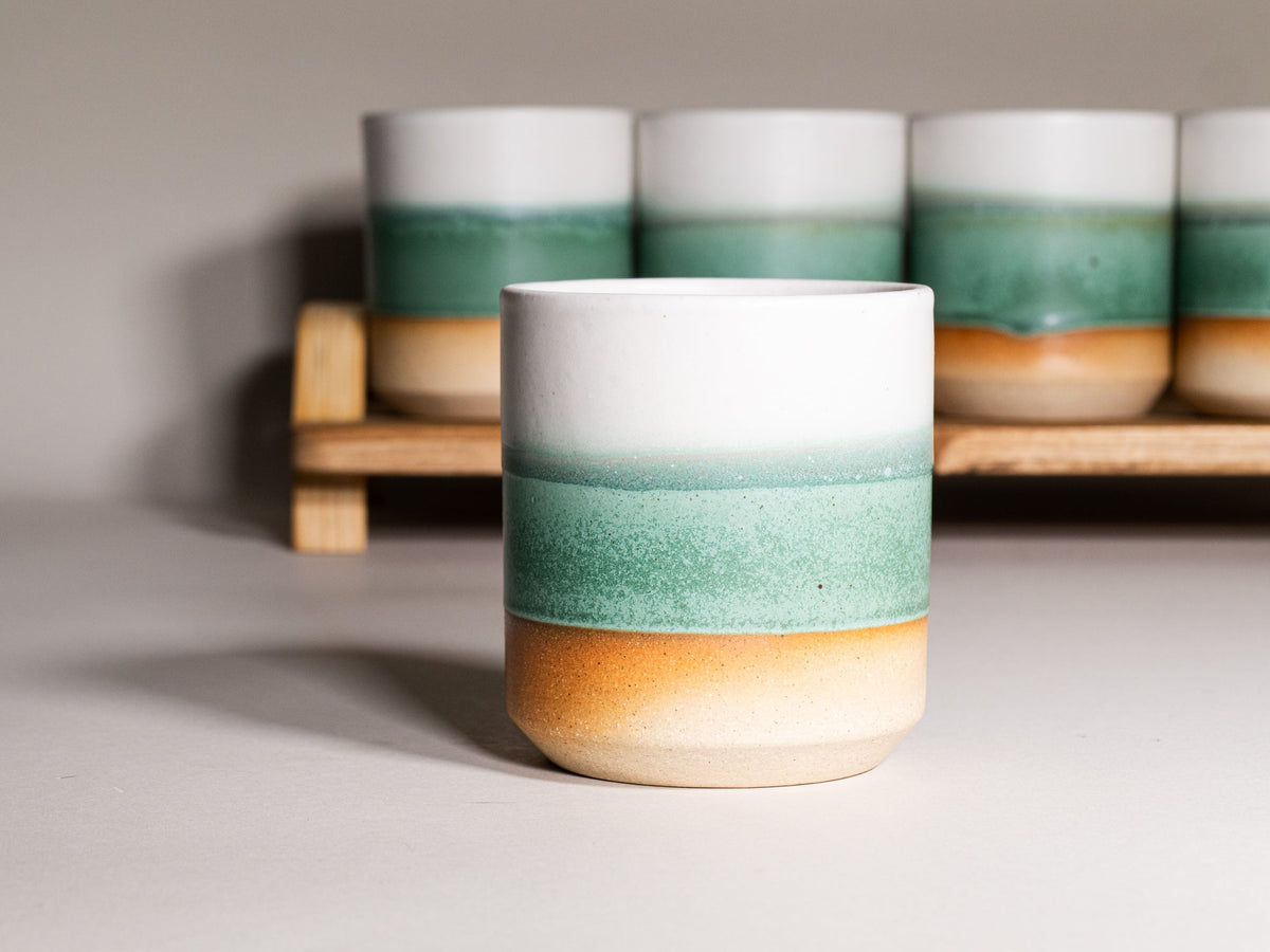 Green and white stoneware smoothie cup, 14 oz, centered with multiple cups behind.