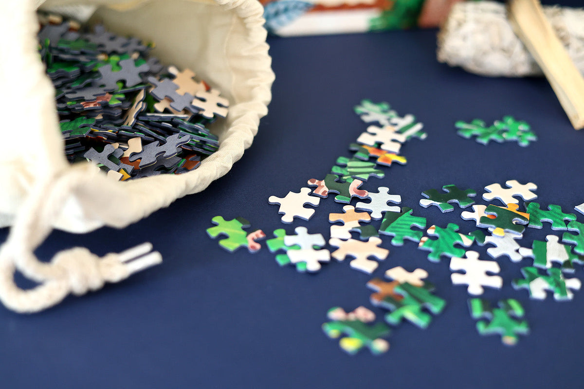 Assorted jigsaw puzzle pieces spread on tabletop near a fabric bag