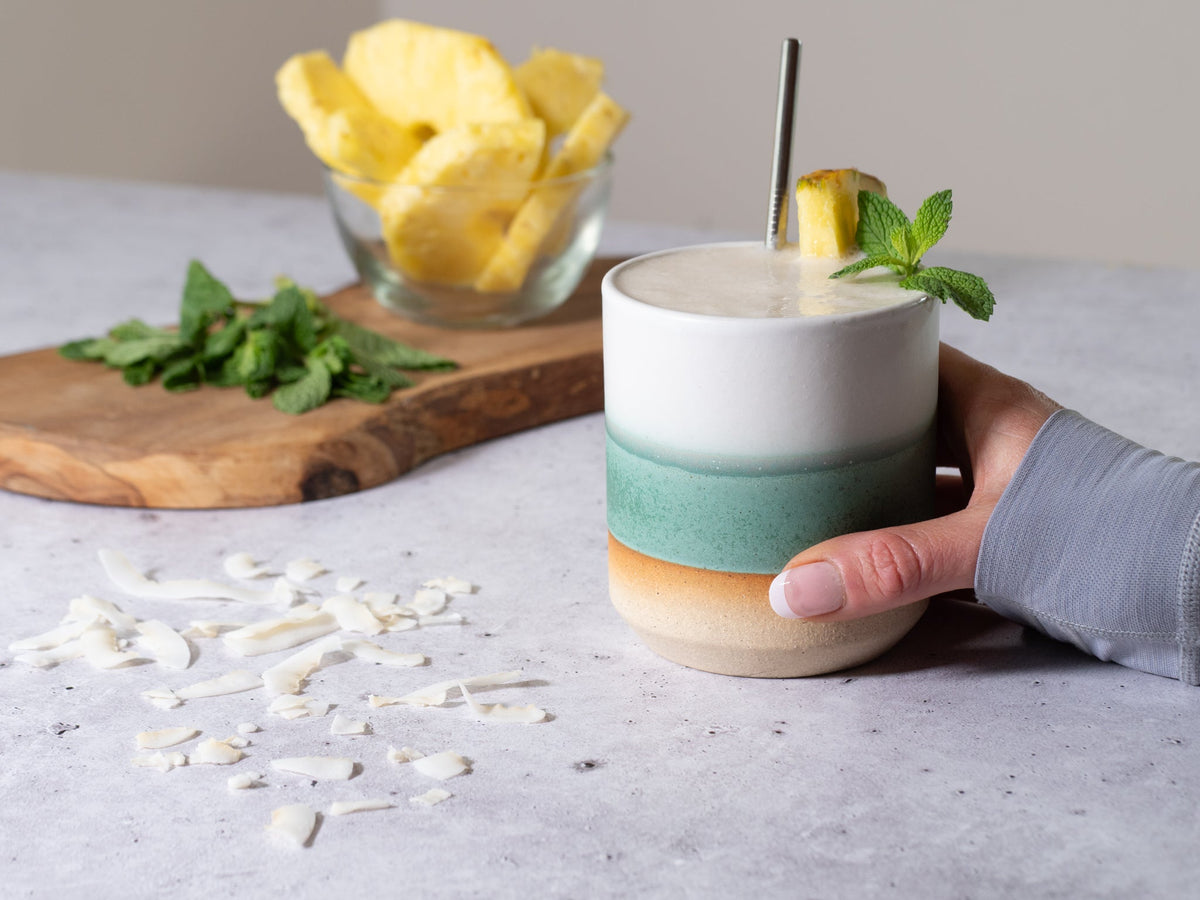 Green and white stoneware smoothie cup, 14 oz, held in hand with straw.