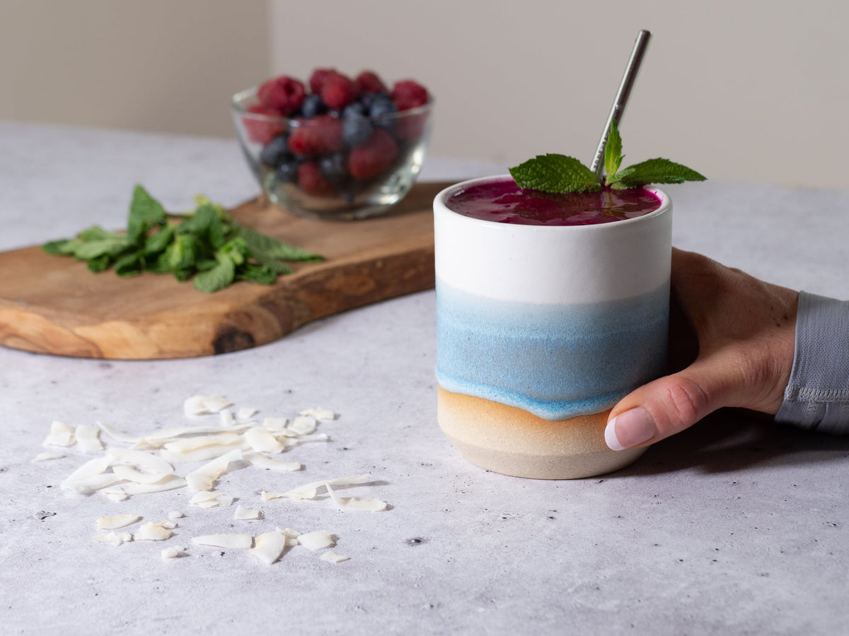 Ice blue and white stoneware smoothie cup with red berry smoothie, held by hand