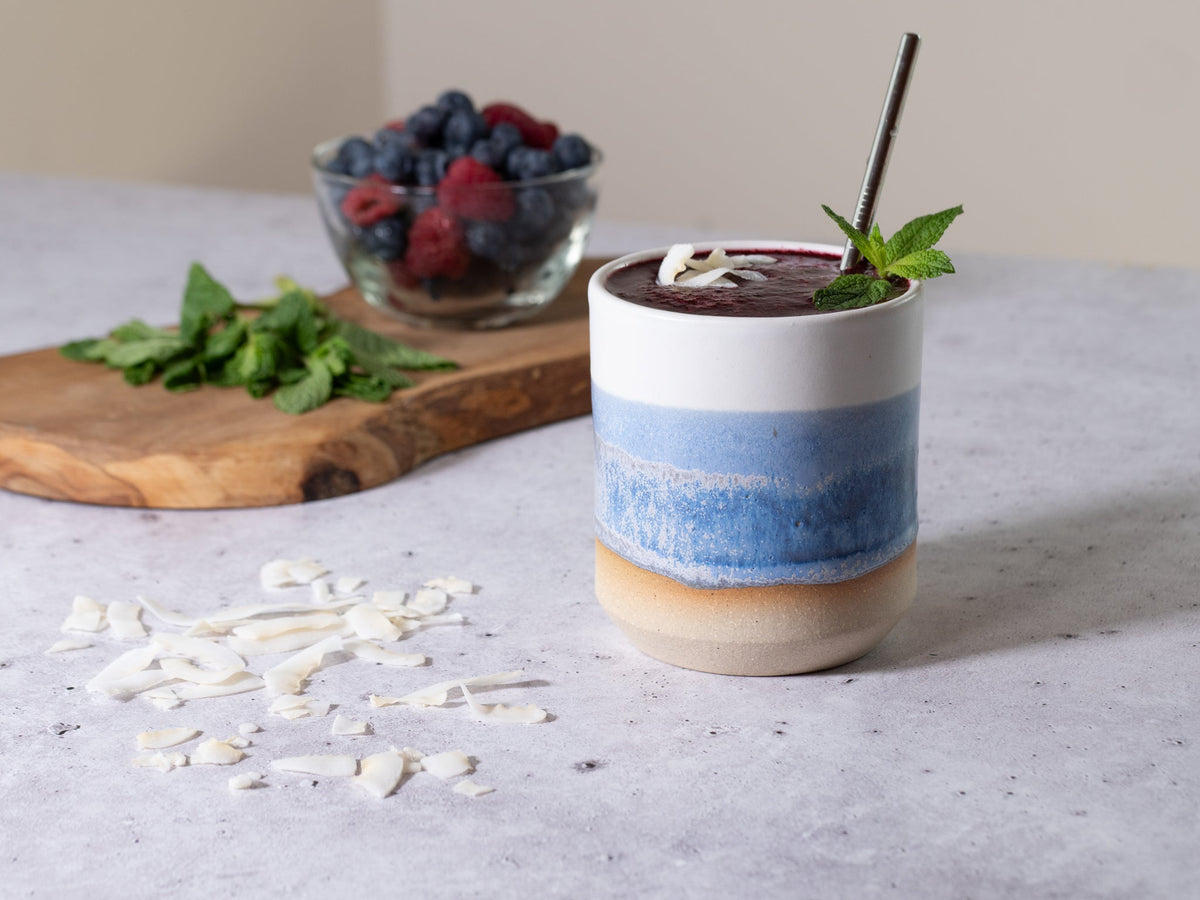 Stoneware smoothie cup with blue band, filled smoothie with mint and straw garnish