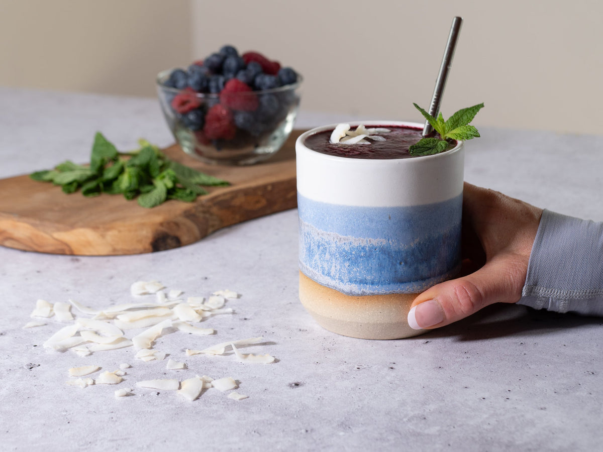 Stoneware smoothie cup with blue band, held by hand, smoothie with mint leaf garnish