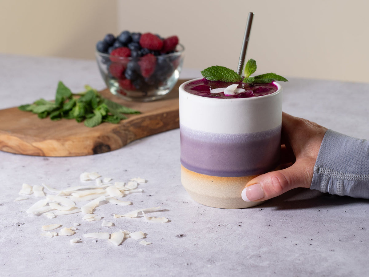 Hand holding a stoneware smoothie cup with purple-white ombre glaze and mint garnish