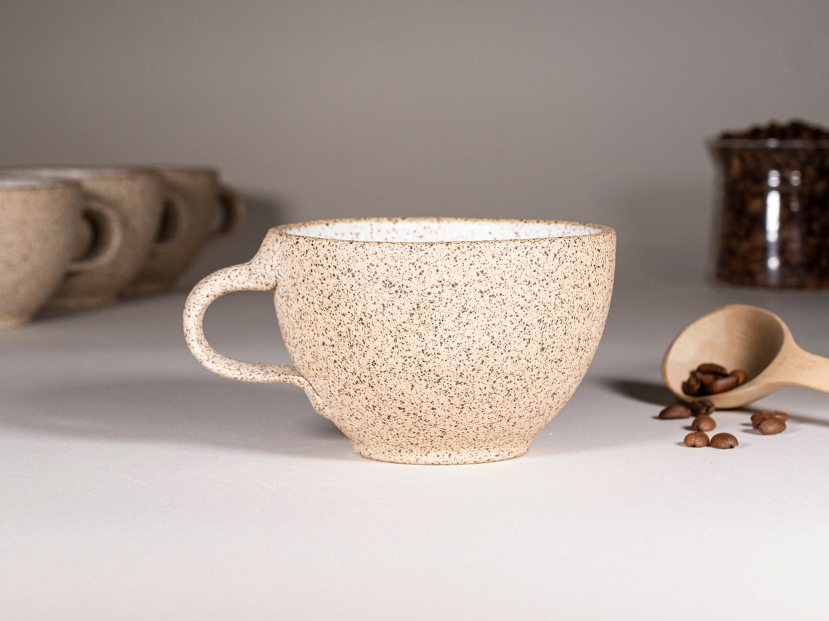 Speckled stoneware latte cup with curved handle, on matching saucer