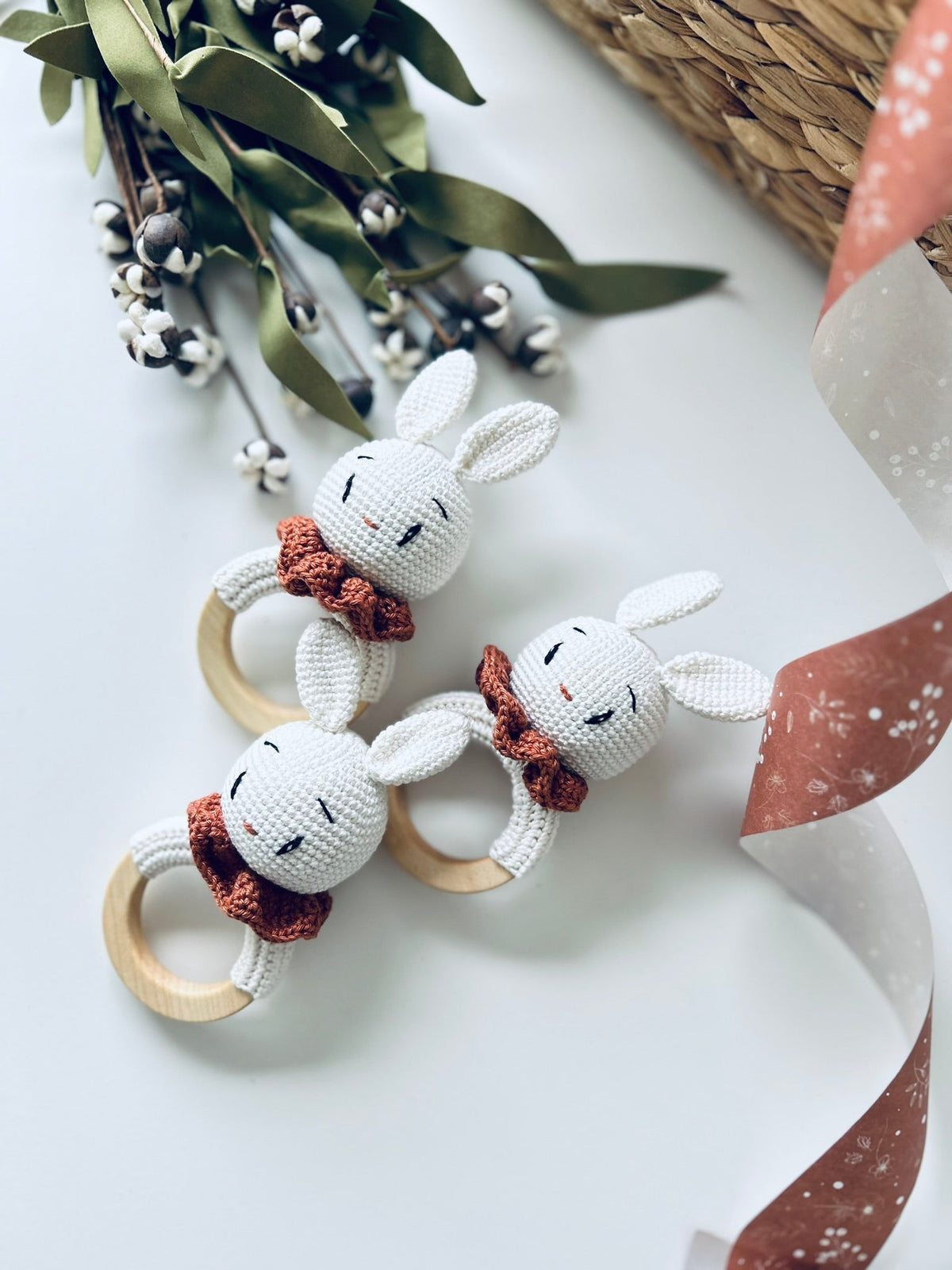 Three crocheted bunny rattle teethers with orange scarves and wooden ring handles