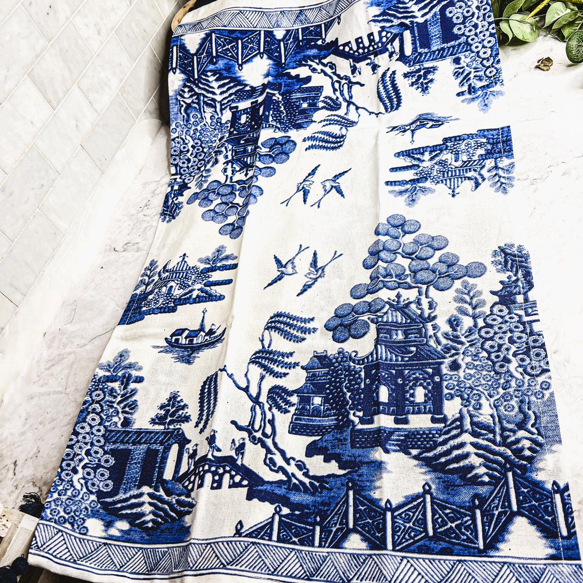 Blue-and-white chinoiserie tea towel featuring a detailed landscape scene and fringe
