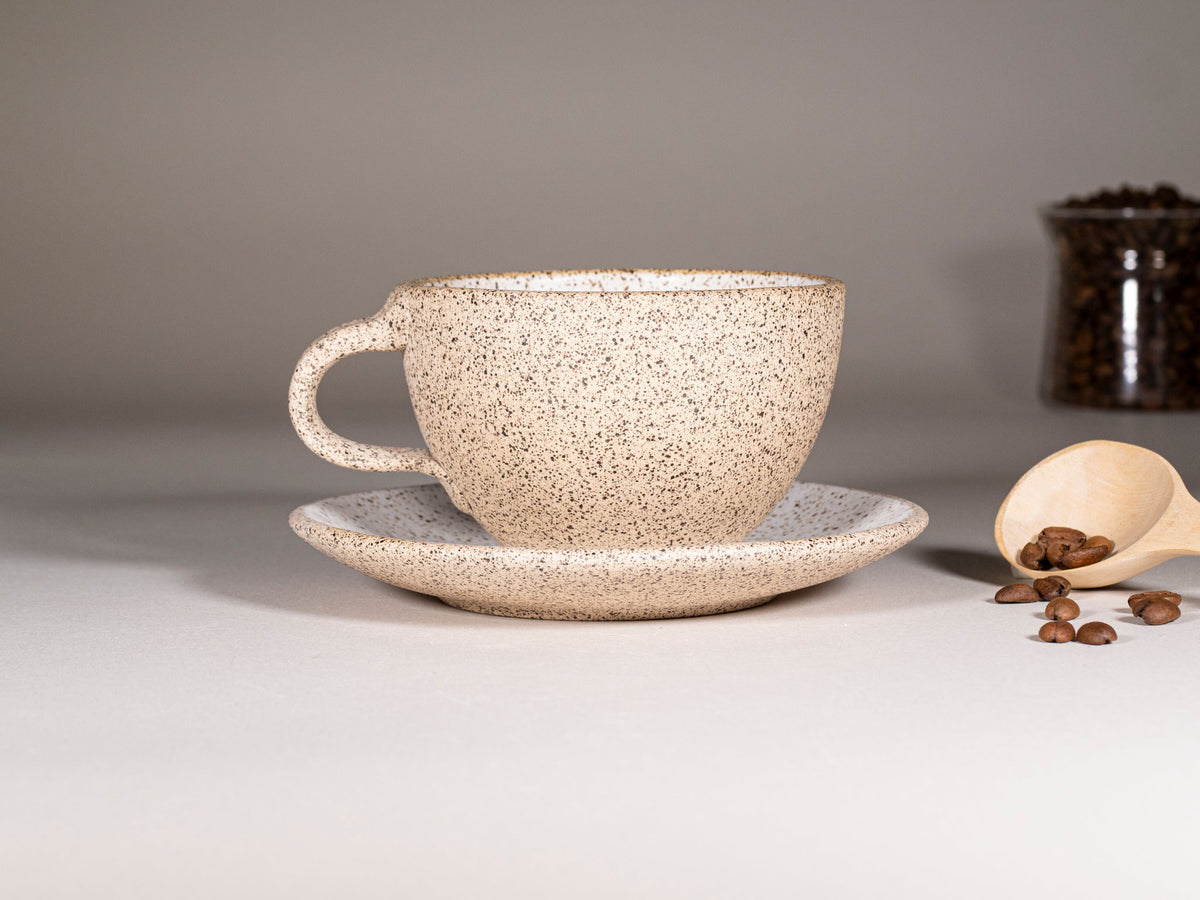 Speckled stoneware latte cup with handle and matching saucer on tabletop