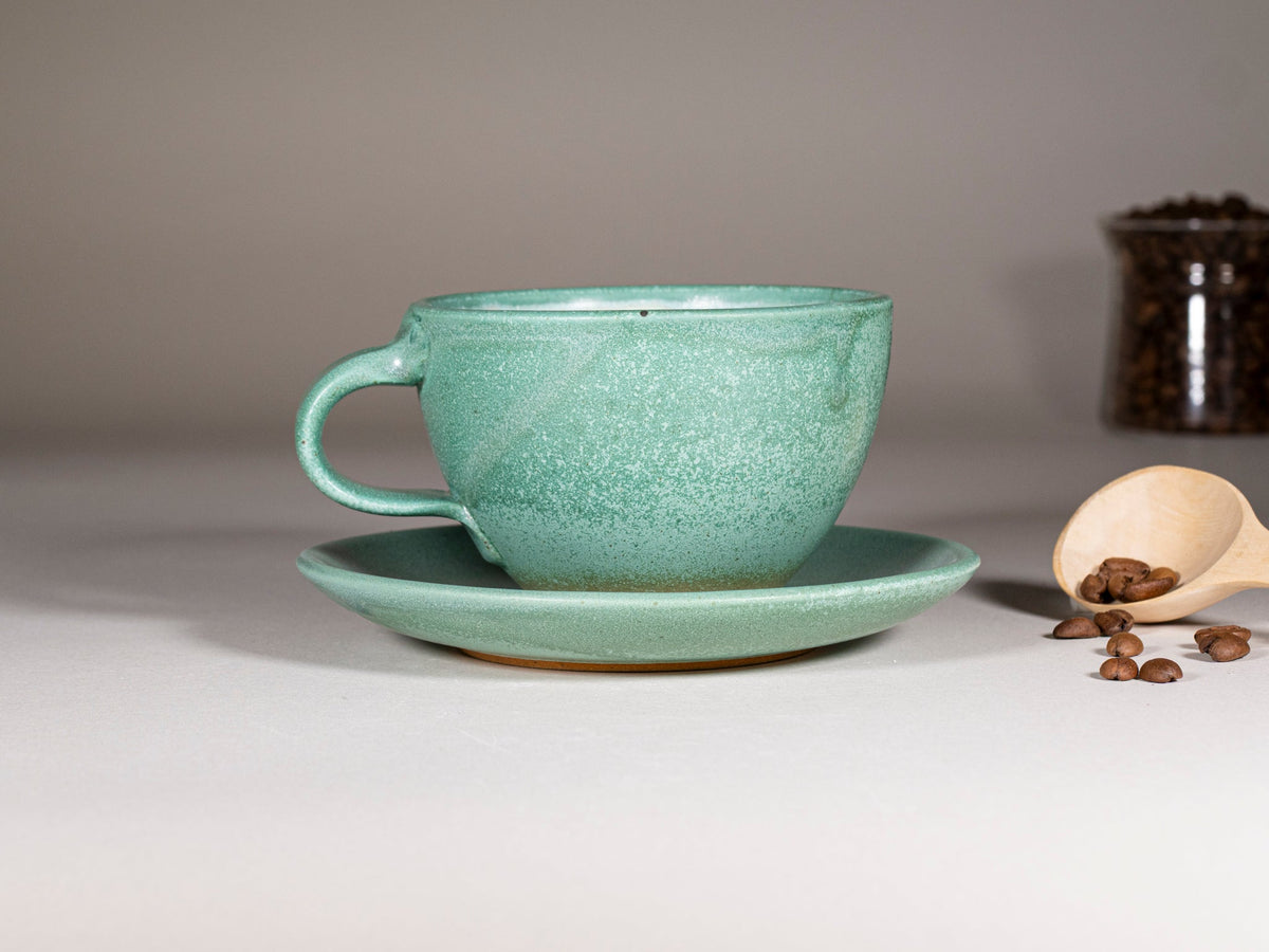 Green stoneware latte cup with handle and matching saucer, textured speckled glaze