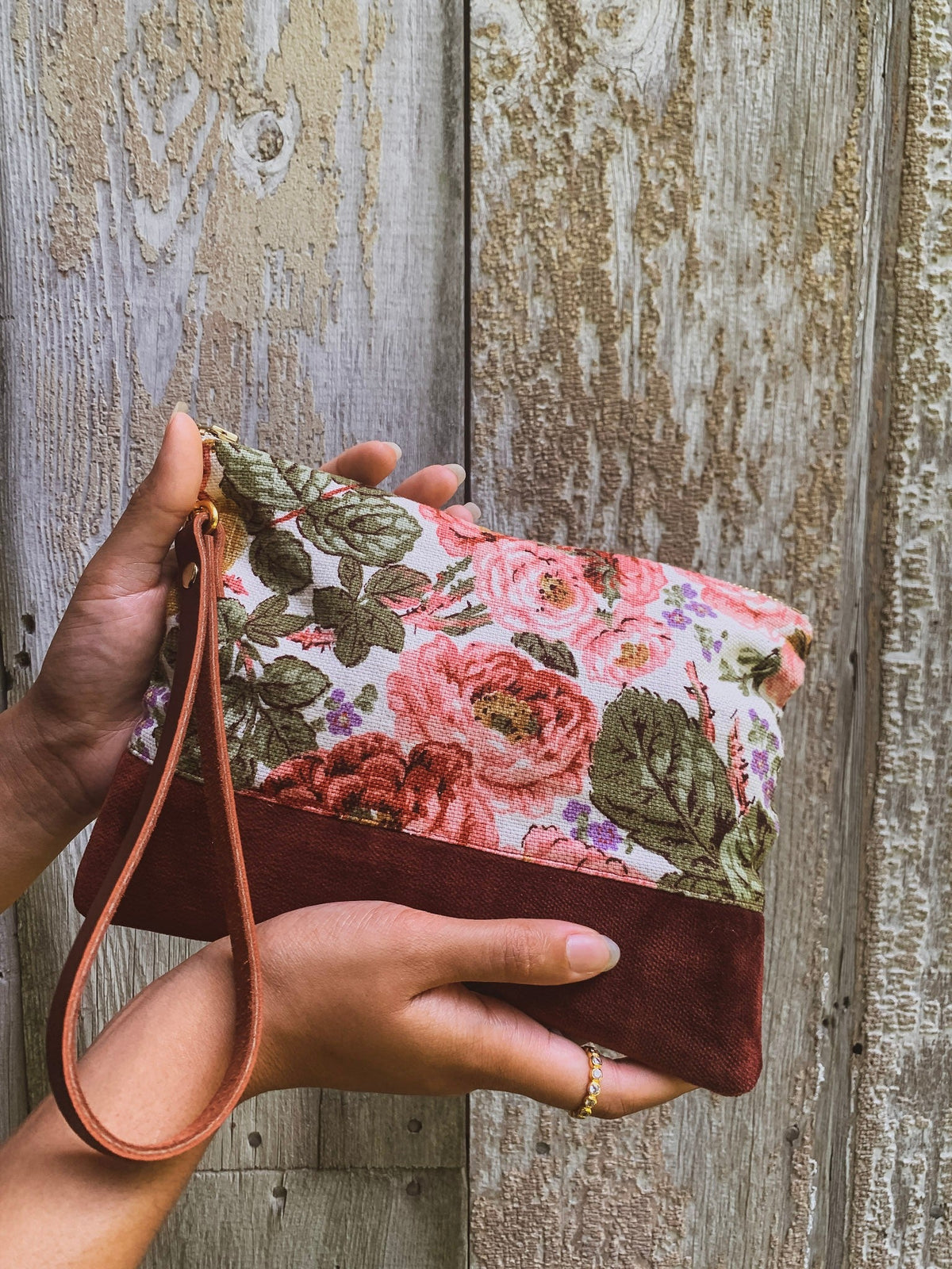 Floral wristlet purse with brown suede flap, wrist strap, and gold hardware detail.