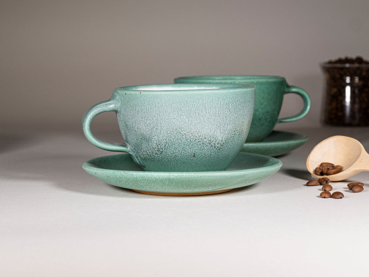 Green stoneware cup with handle and matching saucer set, speckled glaze finish.