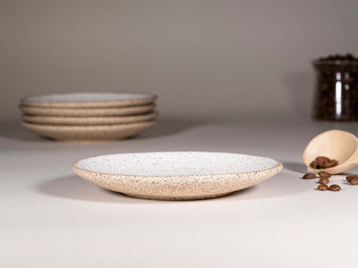 Speckled stoneware saucer with stacked saucers in background, white speckle