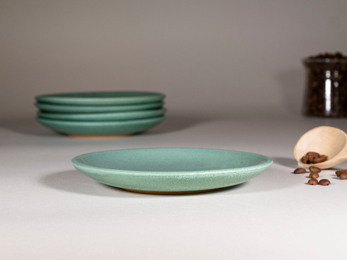 Green speckled stoneware saucer plates, stacked, smooth curved rim.