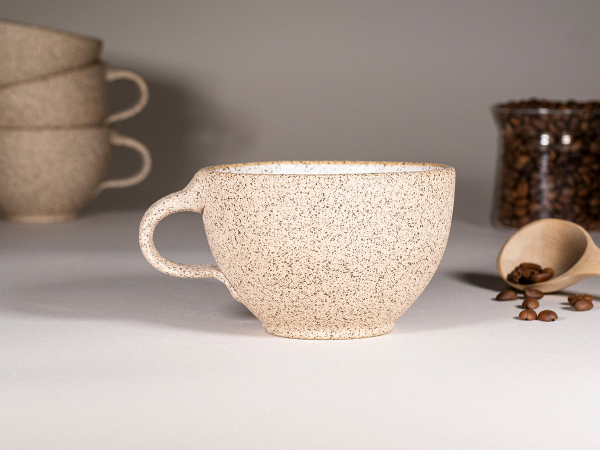 Speckled stoneware latte cup with side handle, set on a matching saucer
