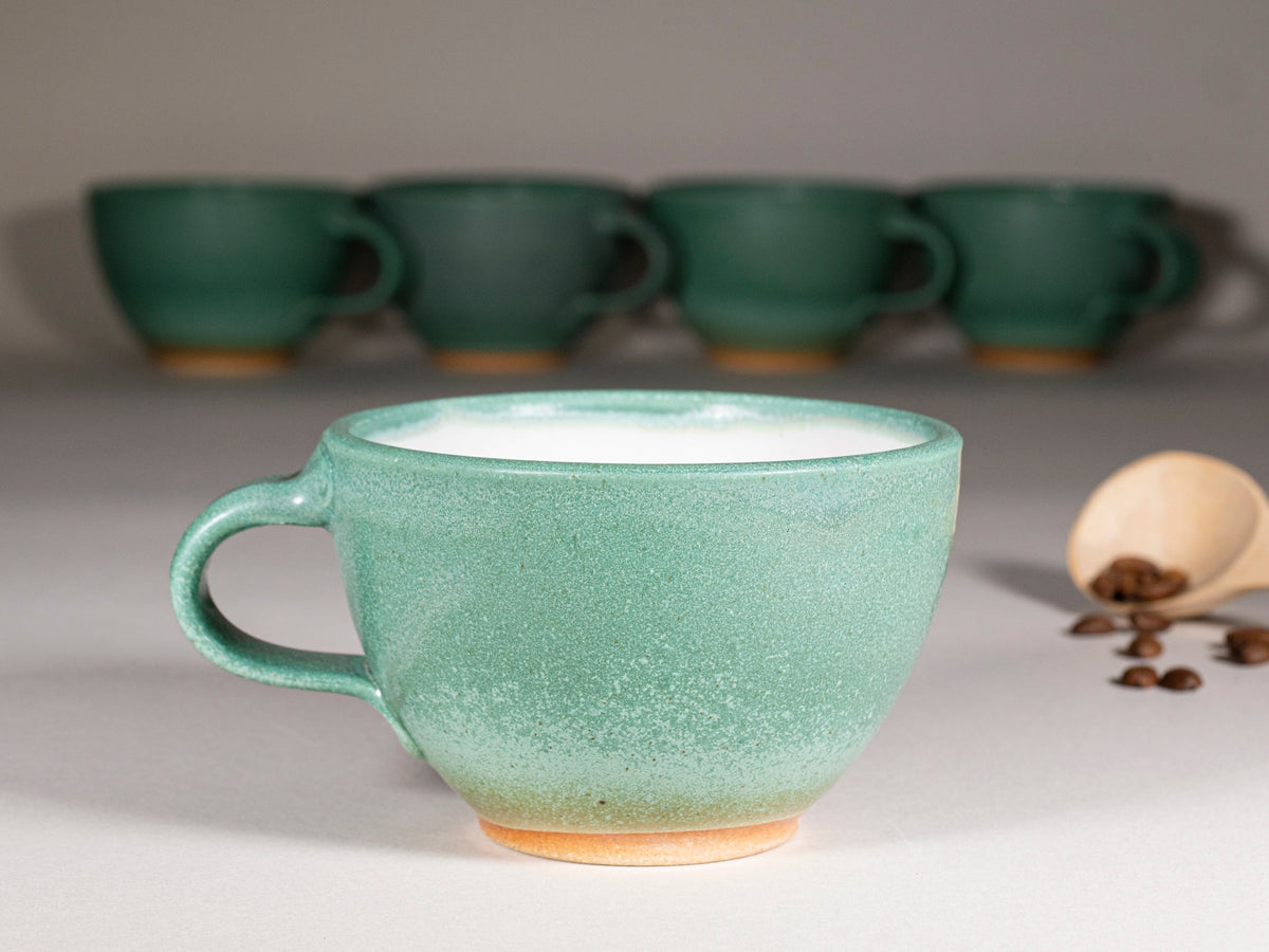 Green stoneware latte cup with handle, speckled glaze; multiple cups behind