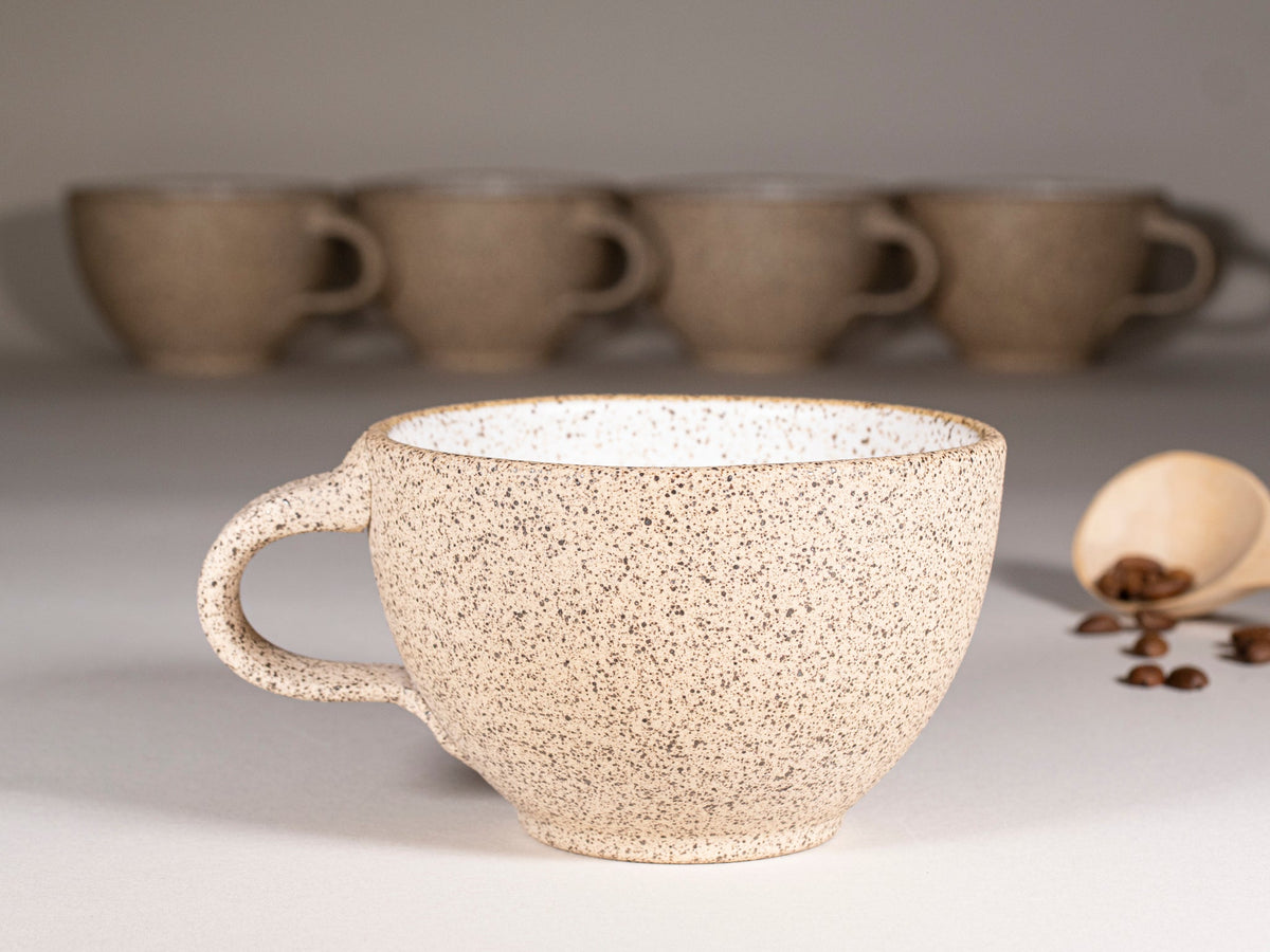 Speckled stoneware latte cup with handle, served with matching saucer