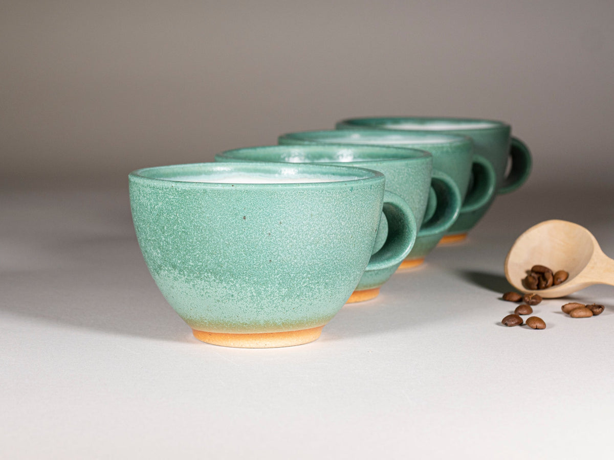 Green stoneware latte cup with handle, speckled glaze; stacked cups behind