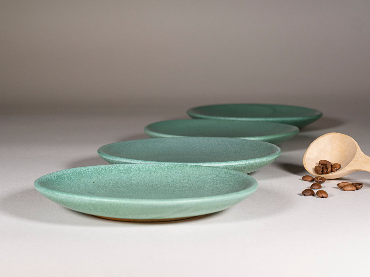 Stacked green stoneware cups and saucers, speckled glaze, rounded handles.