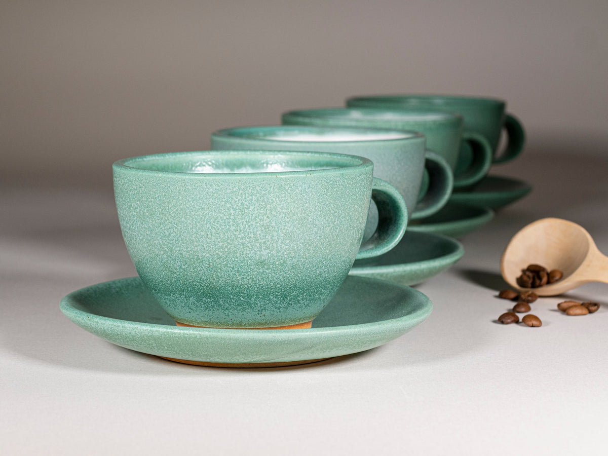 Green speckled stoneware latte cups with matching saucers, each with a handle.