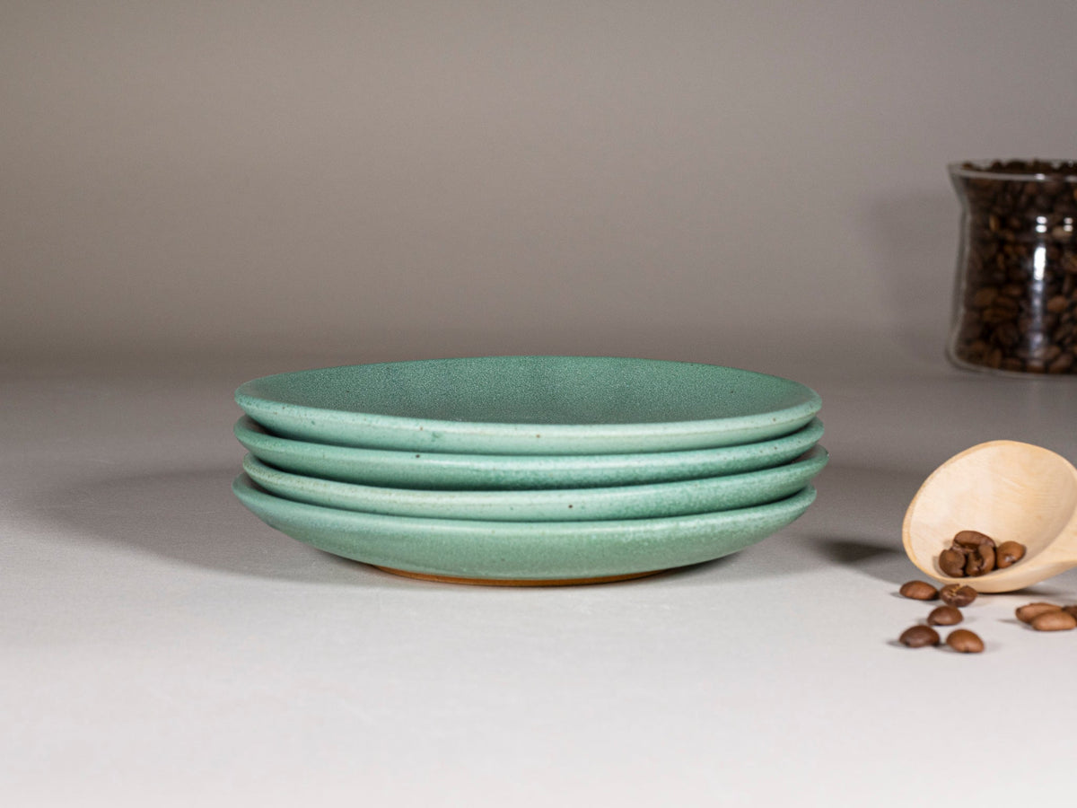 Stack of green speckled stoneware saucers with matching glaze finish.