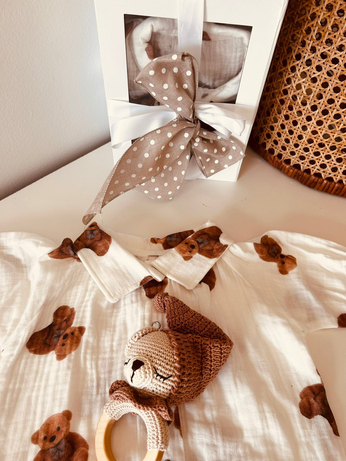 Teddy bear rattle resting on bear-print baby romper beside a bow-tied gift box