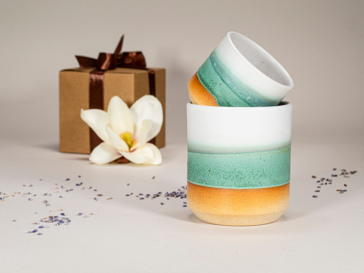 Green-and-white stoneware espresso cup with layered bands, another cup slightly behind