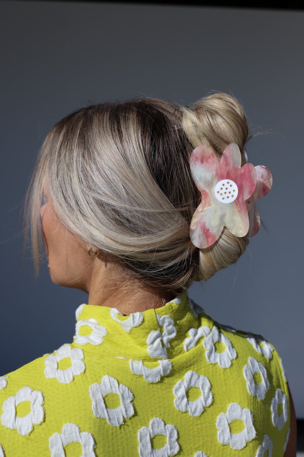 Pink translucent floral hair claw clip with white polka-dot center on bun