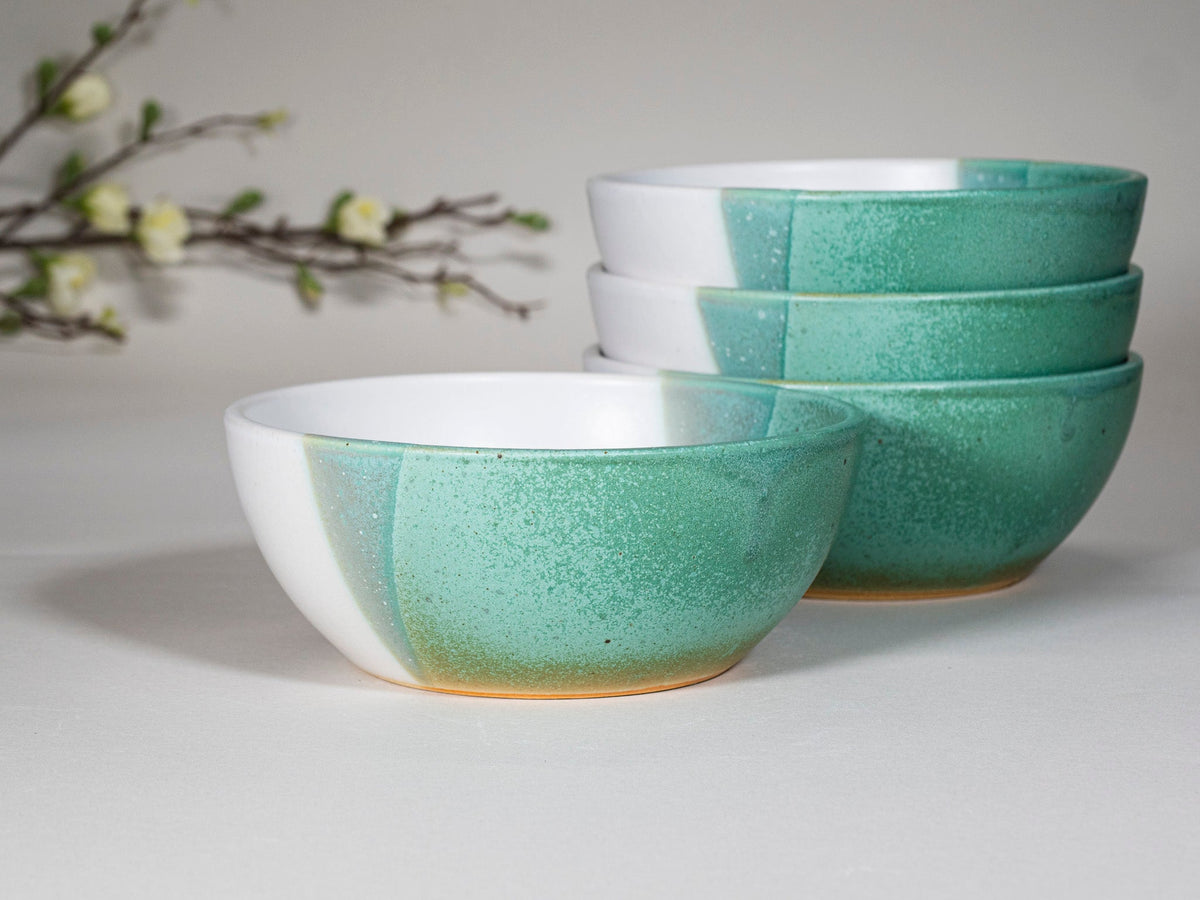 Stacked handmade stoneware soup bowls with speckled green glaze and white exteriors
