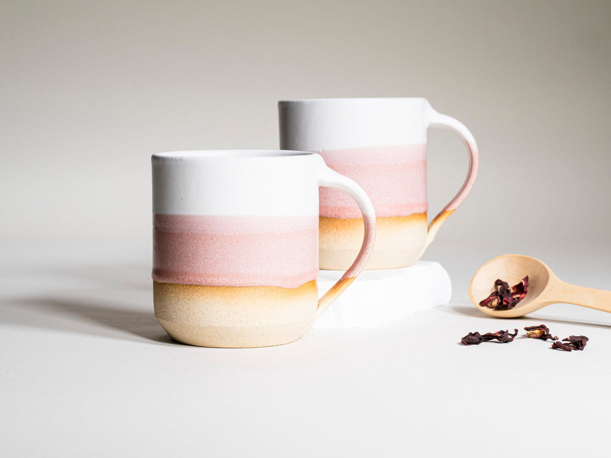 Two pink-and-white striped ceramic coffee mugs with handles on a tabletop