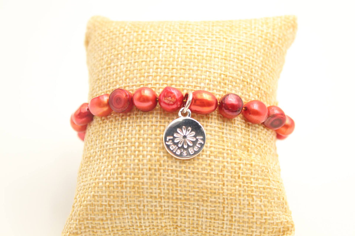 Red pearl bracelet with a silver-tone floral charm, displayed on a cushion