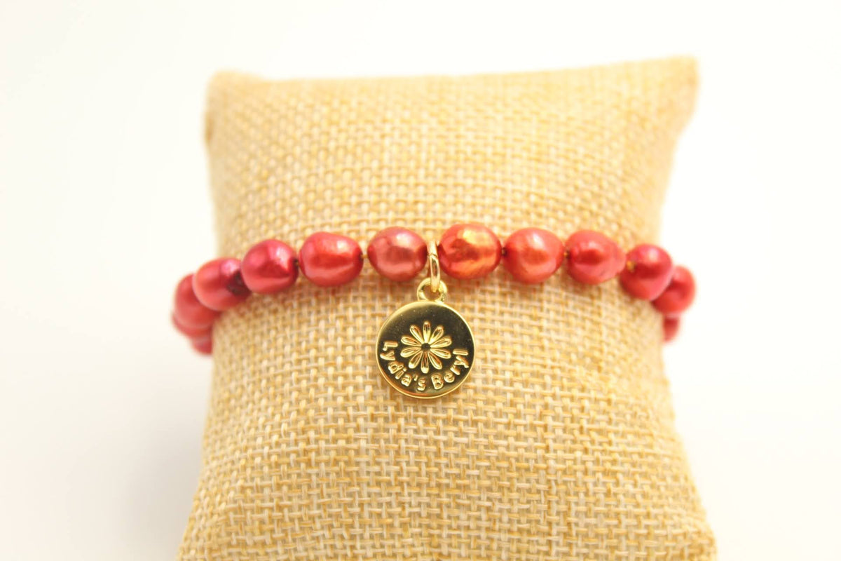 Red pearl bracelet with a gold-tone floral charm, displayed on a cushion