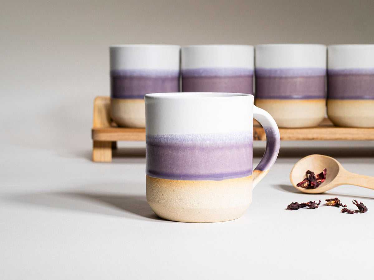 14 oz purple and white ceramic coffee mug with handle in front, with matching mugs behind.