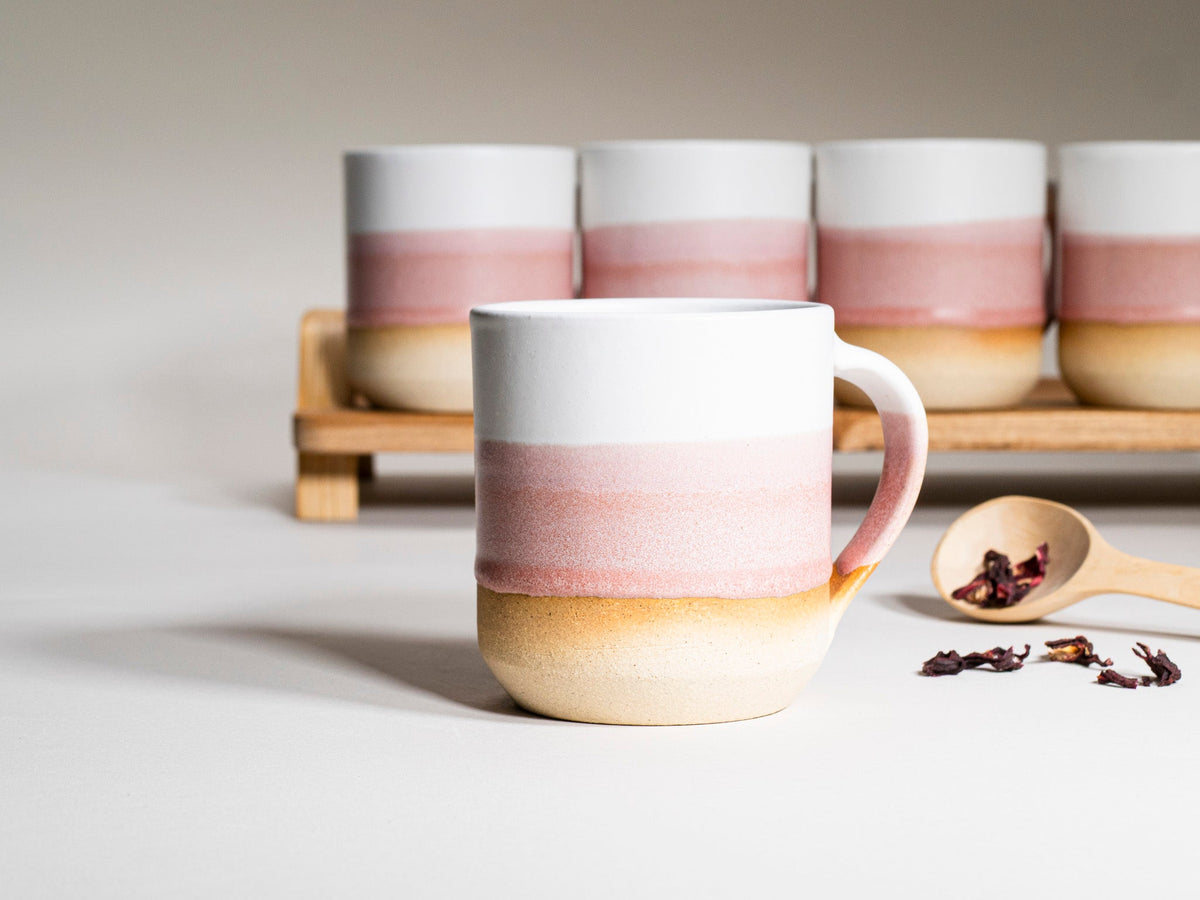 Pink and white striped ceramic coffee mug with handle in front of matching mugs