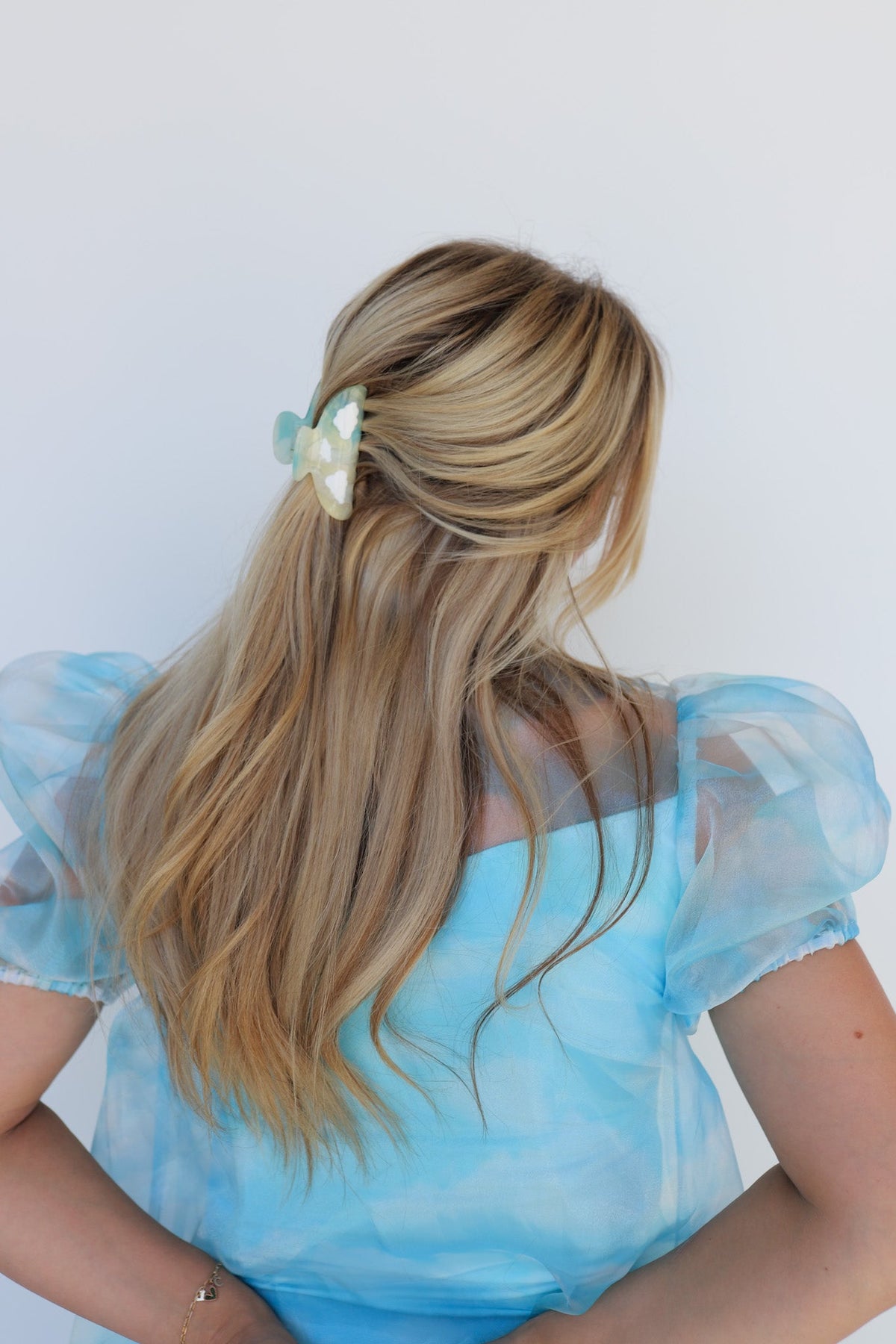 Butterfly-like teal hair claw on long blonde hair; light blue puff-sleeve dress