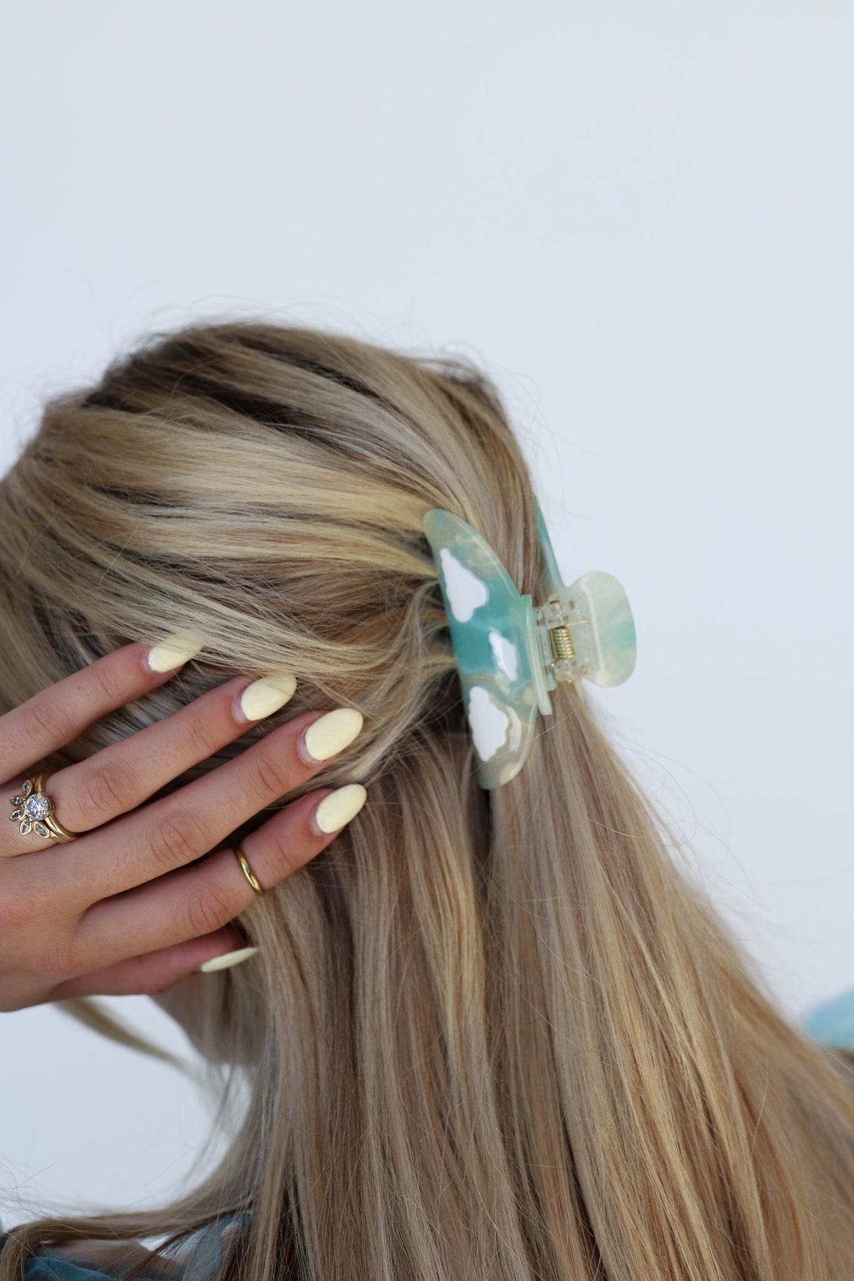 Teal-blue hair claw clip on blonde hair with hand wearing rings